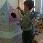 Chłopiec koloruje kartonowy domek